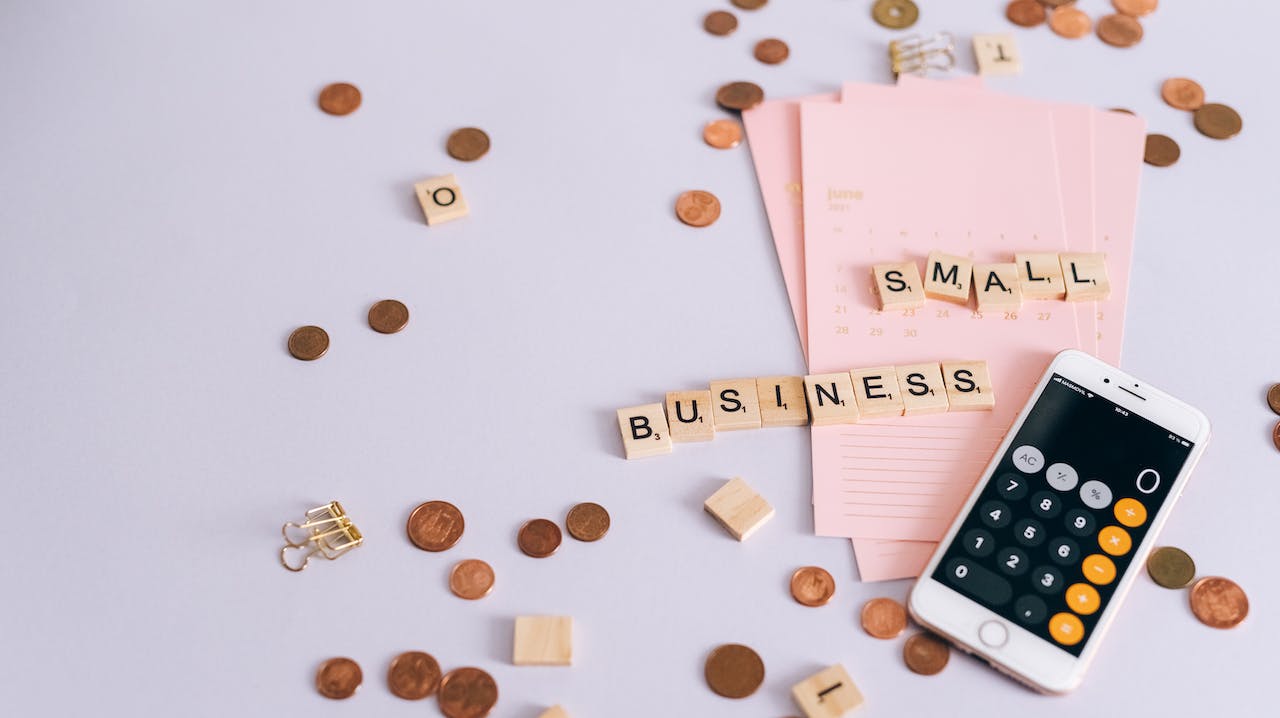 image of coins on a table while scrabble tiles spell small business and a phone calculator is showing  zero